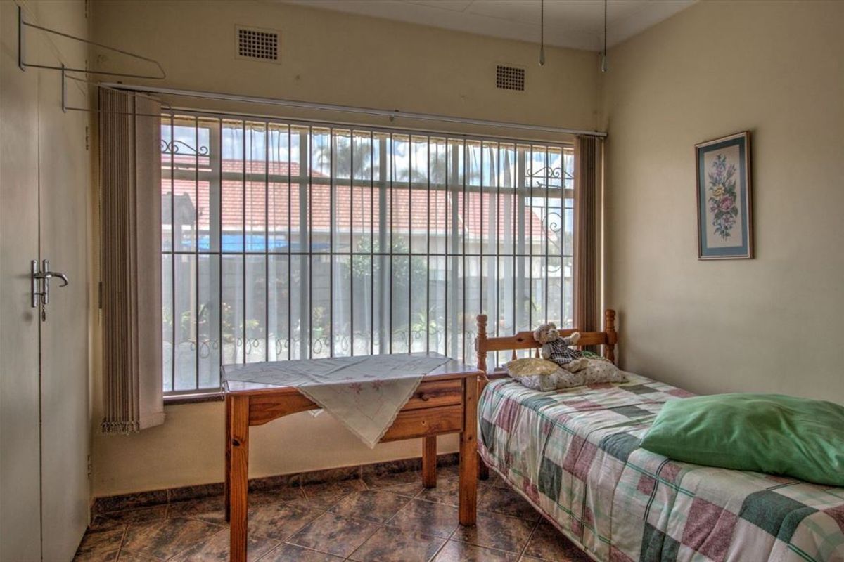 A bedroom featuring tiled flooring, built-in cupboards, and a large window fitted with security bars.