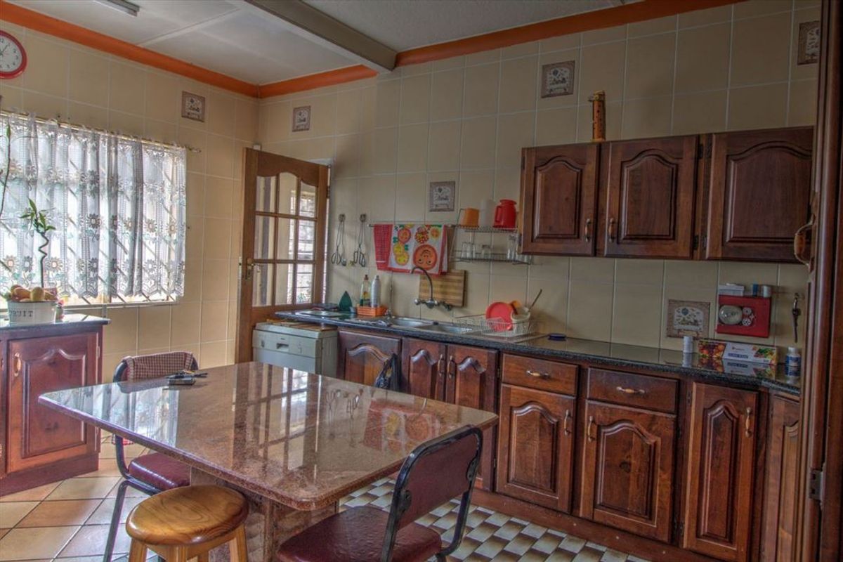 A dated kitchen featuring traditional dark wood cabinetry, tiled walls, and a stone-topped dining area, offering a functional layout with potential for modernization.