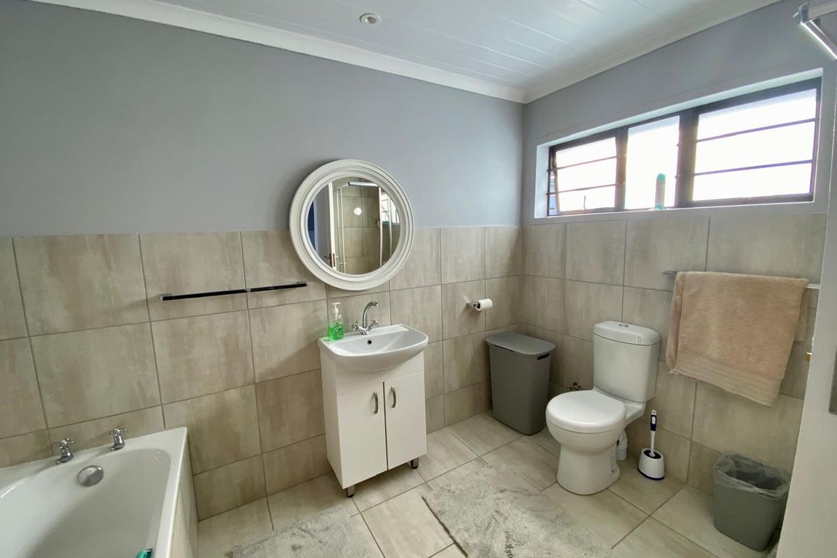 A functional bathroom featuring a built-in bathtub, a pedestal vanity with basin, and a standard toilet, finished with neutral wall and floor tiling.
