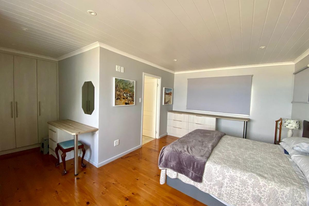 Spacious bedroom featuring polished timber flooring, built-in cabinetry, and a neutral color palette with recessed ceiling lighting.
