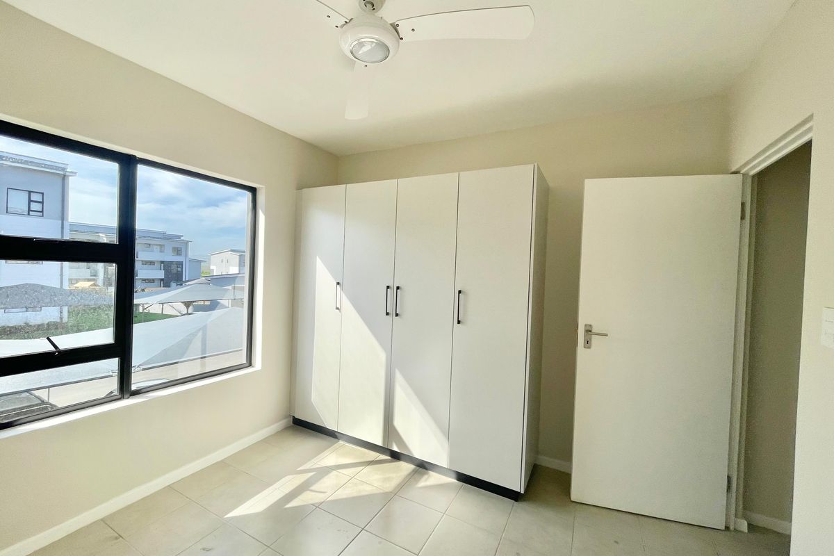 A bright, empty bedroom featuring tiled flooring, a built-in wardrobe, and a ceiling fan, offering a clean and neutral living space.
