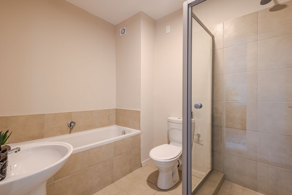 A clean, functional bathroom featuring a built-in bathtub, a separate glass-enclosed shower, a pedestal basin, and a toilet with neutral wall and floor tiling.