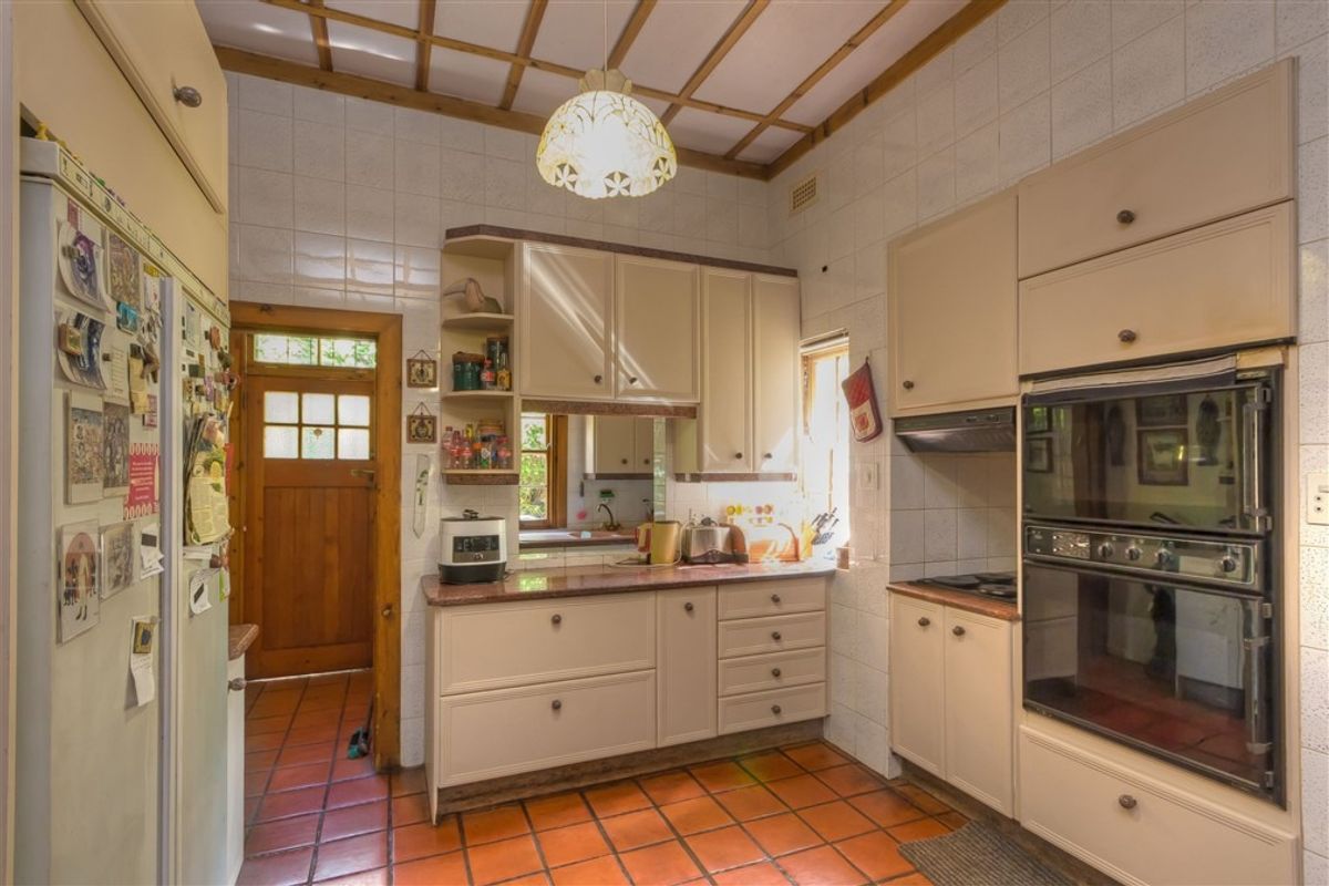 A dated kitchen featuring original cabinetry, built-in double oven, tiled flooring, and wall-to-wall tiling, offering potential for a modern renovation.