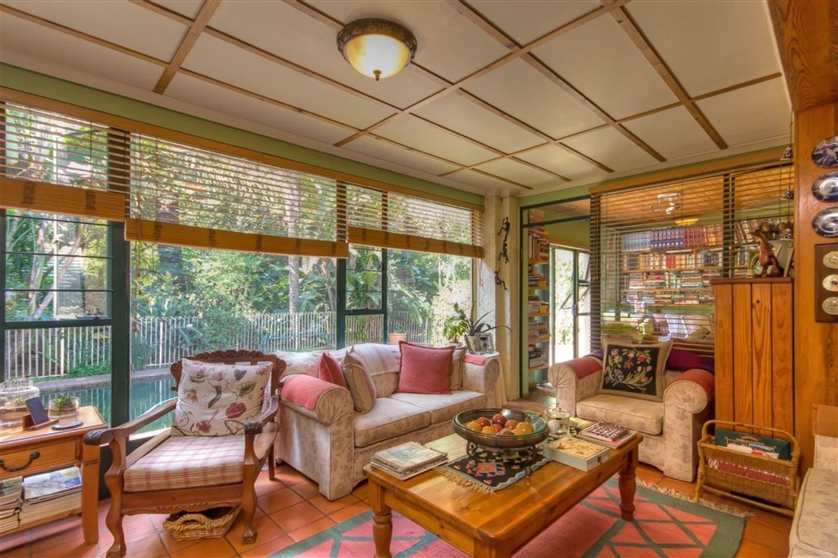 A cozy living room featuring large windows with garden views, terracotta floor tiles, and a unique coffered ceiling design.