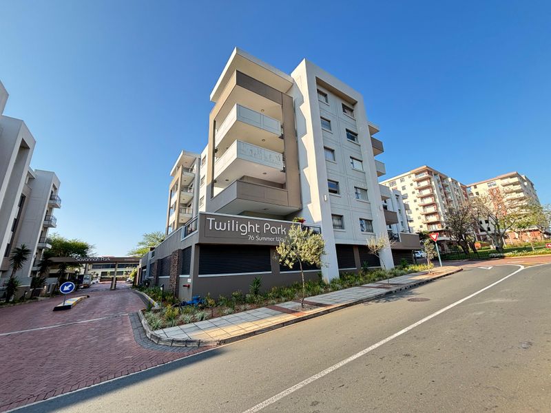 Exterior view of the Twilight Park apartment complex, showcasing modern architectural design, balconies, and secure gated entrance access from the street.