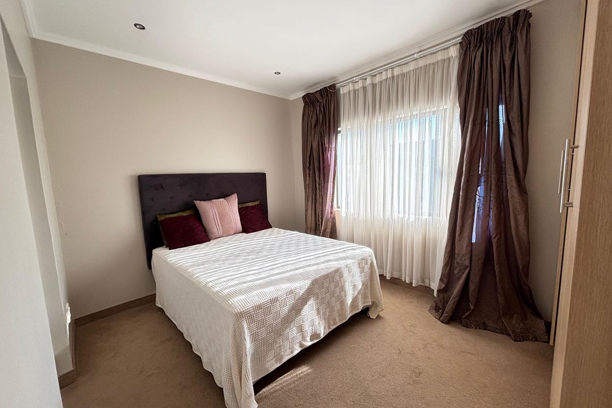A well-lit bedroom featuring neutral wall tones, fitted carpeting, and recessed ceiling lighting, providing a comfortable and functional living space.