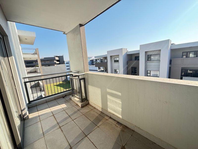 A private apartment balcony featuring tiled flooring and metal railings, offering an open view of the surrounding residential complex.