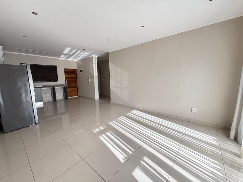 An open-plan living and kitchen area featuring polished floor tiles, recessed ceiling lighting, and a neutral color palette.