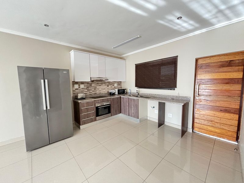 Modern kitchen featuring two-tone cabinetry, granite countertops, built-in oven, hob, extractor fan, and tiled flooring with direct access to the living area.