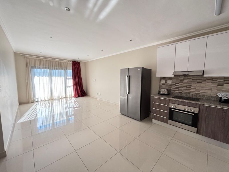 Open-plan living area featuring tiled flooring, recessed lighting, and a modern kitchen with built-in oven, hob, extractor fan, and sleek cabinetry.