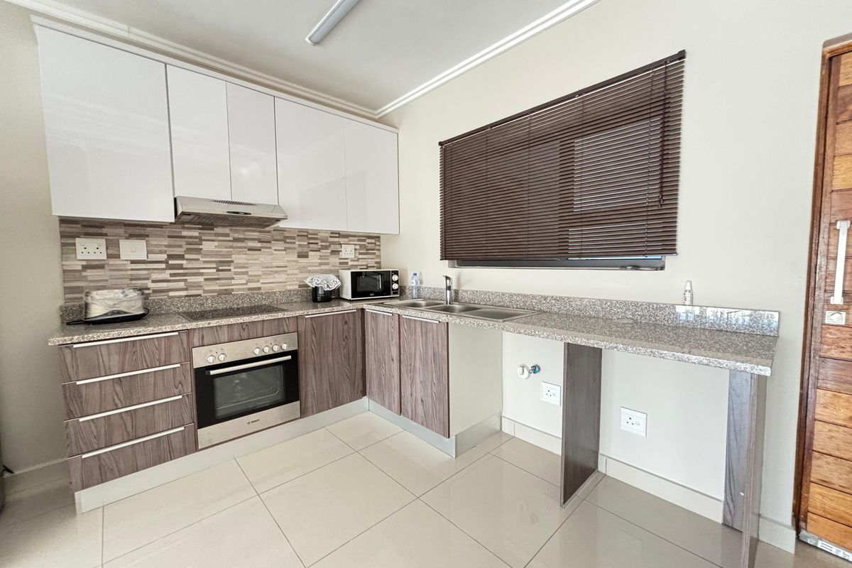 Modern kitchen featuring two-tone cabinetry, granite countertops, a built-in oven, extractor fan, and tiled flooring with a dedicated space for an under-counter appliance.
