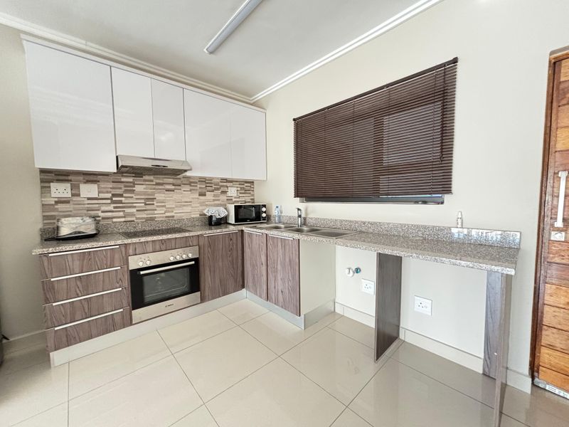 Modern kitchen featuring two-tone cabinetry, granite countertops, a built-in oven, extractor fan, and tiled flooring with a dedicated space for an under-counter appliance.