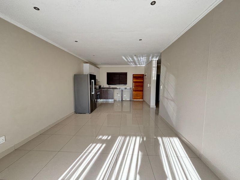Open-plan living area featuring tiled flooring, recessed ceiling lighting, and a compact kitchen with built-in cabinetry and a wooden entrance door.