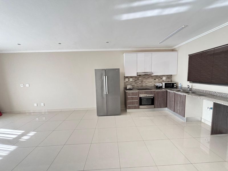 Open plan kitchen featuring modern cabinetry, stone countertops, built-in oven, hob, and extractor fan, set against a spacious tiled living area.