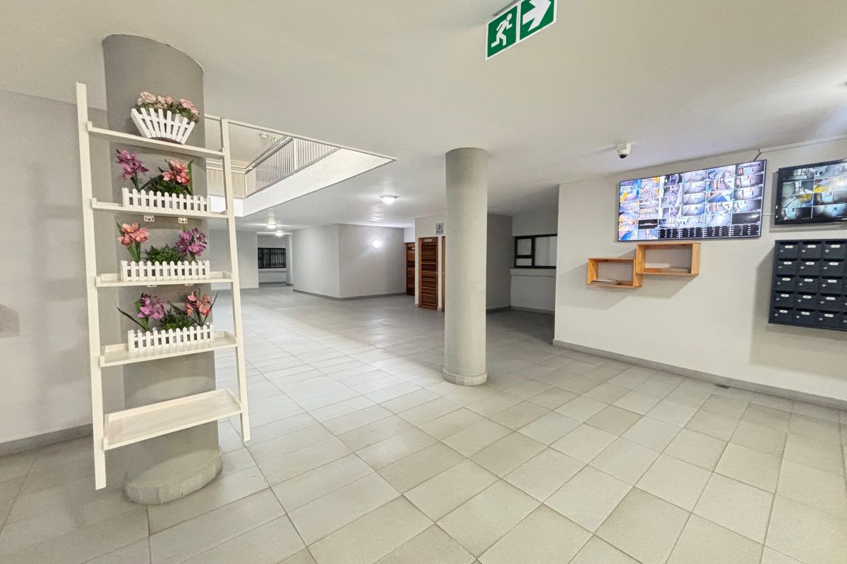 A spacious apartment building lobby featuring tiled flooring, structural columns, a security camera monitor system, and a bank of mailboxes.