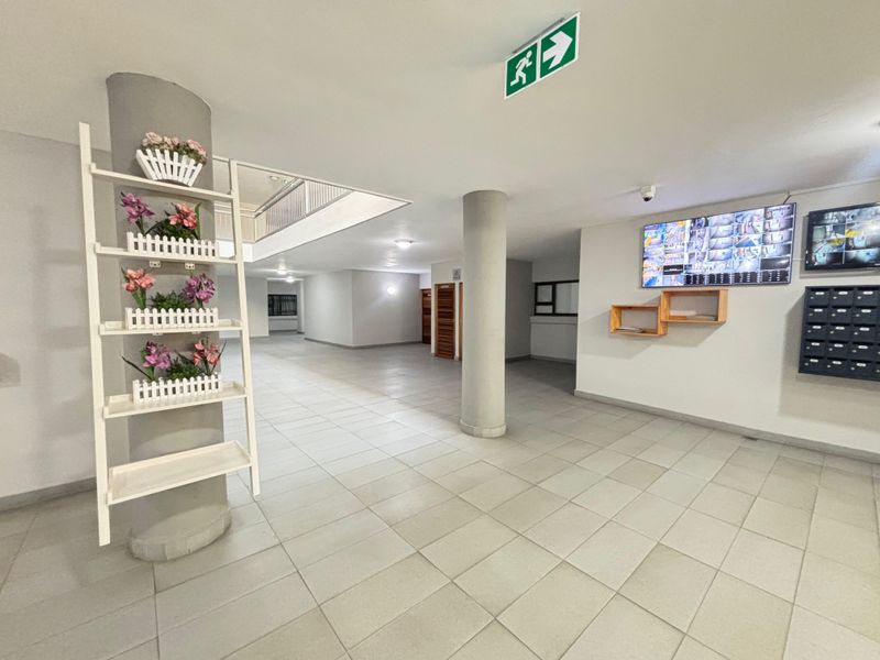 A spacious apartment building lobby featuring tiled flooring, structural columns, a security camera monitor system, and a bank of mailboxes.