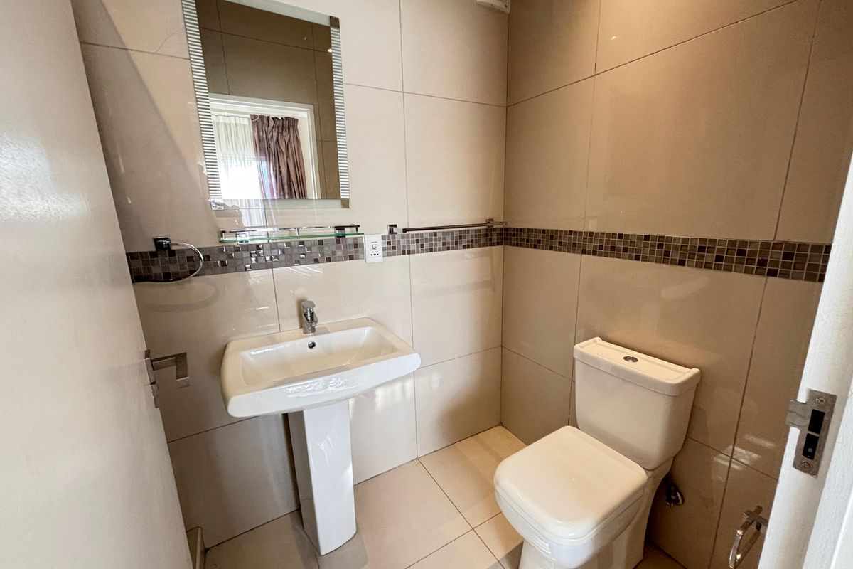 A compact guest bathroom featuring a pedestal basin, modern toilet, and neutral wall tiling with a decorative mosaic border.