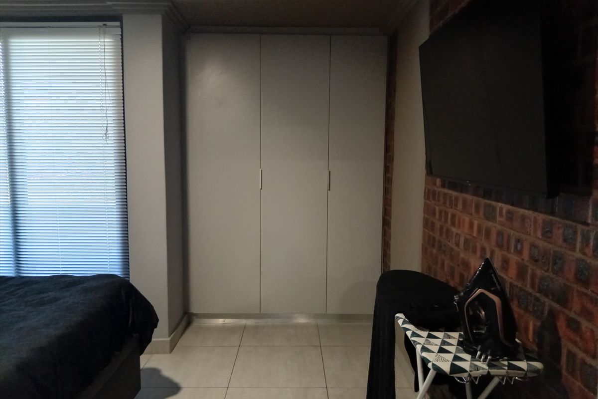 A bedroom featuring built-in floor-to-ceiling wardrobes, tiled flooring, and an exposed brick feature wall.