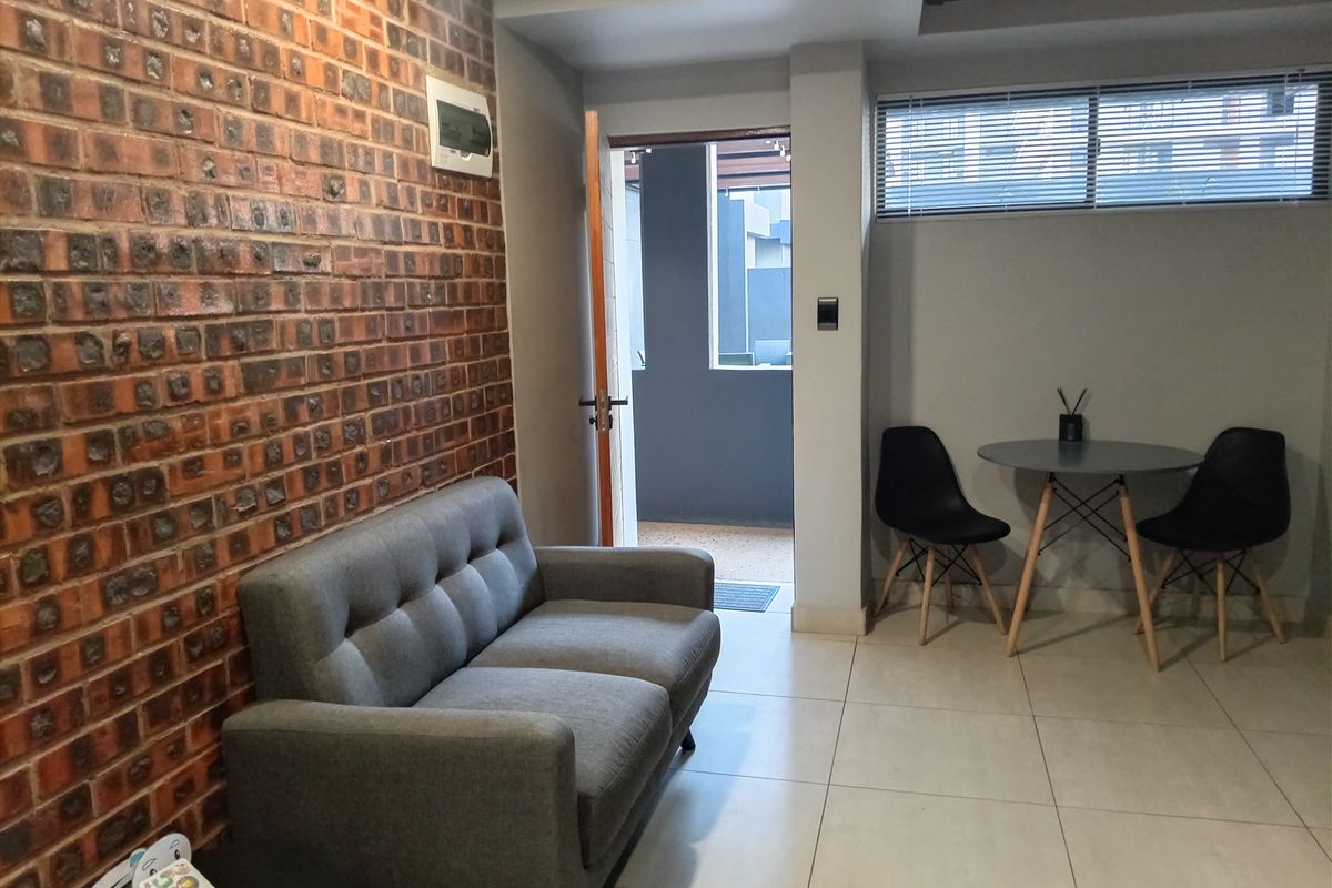 A modern living area featuring a distinctive exposed brick feature wall, large format floor tiles, and direct access to an outdoor patio space.