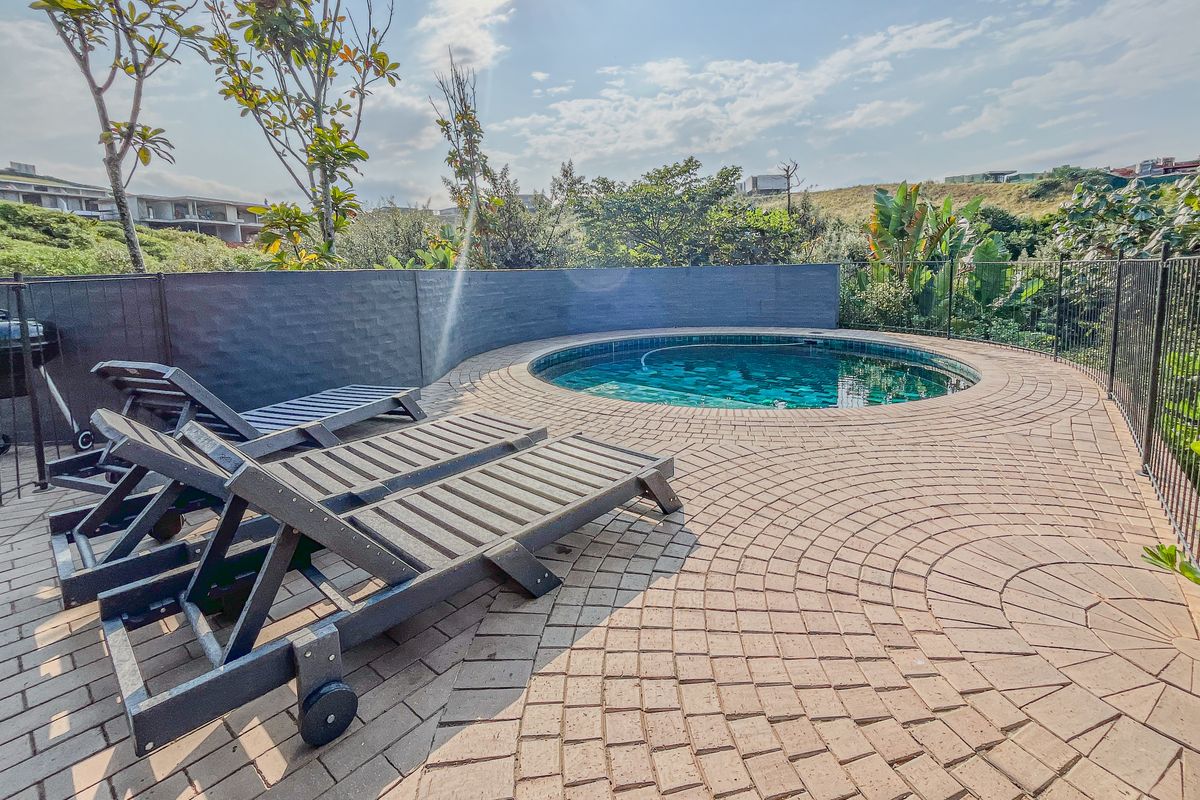 A well-maintained circular swimming pool set within a paved deck area, featuring a retaining wall and secure perimeter fencing.
