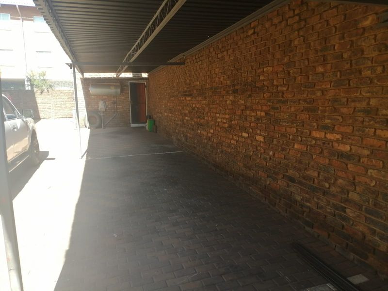 A covered carport area featuring exposed brick walls, paved flooring, and a metal roof structure, providing secure off-street parking.