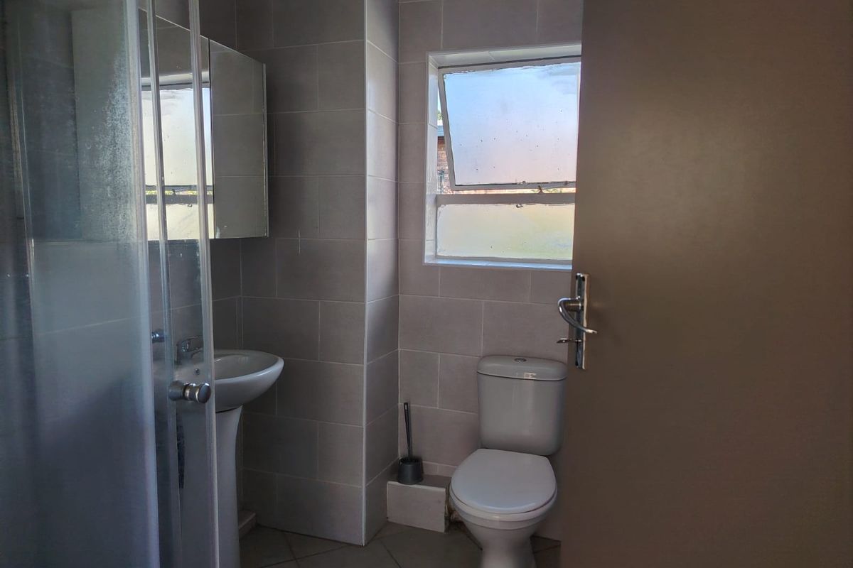 A functional bathroom featuring a pedestal basin, a shower enclosure, and a toilet, finished with neutral wall and floor tiling.