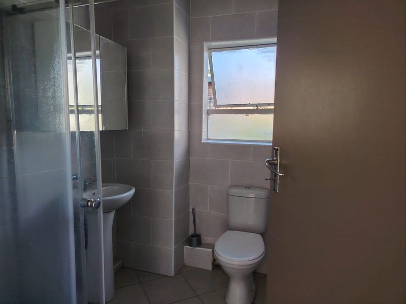A functional bathroom featuring a pedestal basin, a shower enclosure, and a toilet, finished with neutral wall and floor tiling.