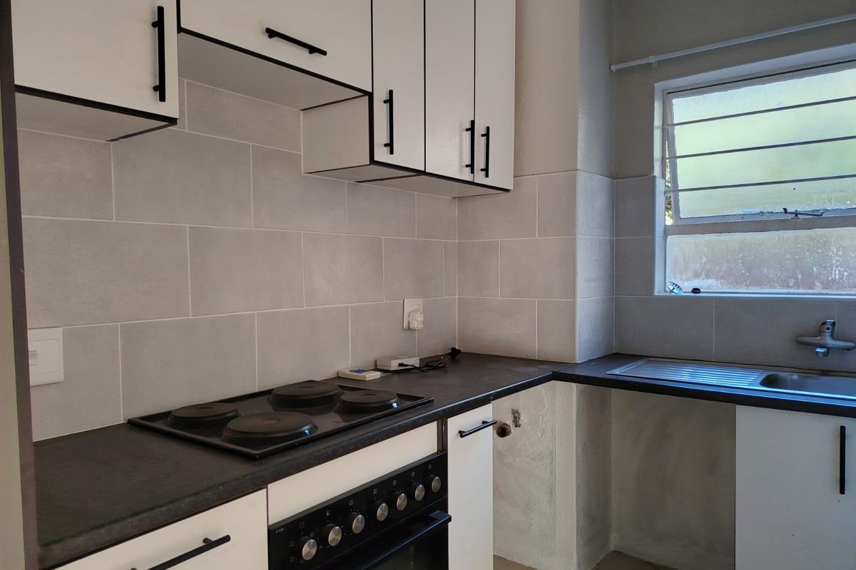 A functional kitchen featuring white cabinetry, dark countertops, a built-in electric stove and oven, and a tiled backsplash with a stainless steel sink.