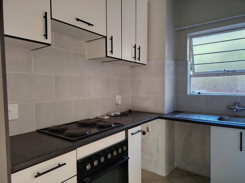 A functional kitchen featuring white cabinetry, dark countertops, a built-in electric stove and oven, and a tiled backsplash with a stainless steel sink.
