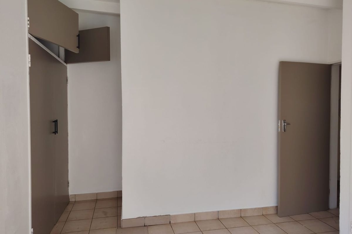 An empty hallway featuring tiled flooring and built-in cupboards, requiring minor repairs to the floor finish.
