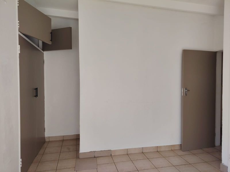 An empty hallway featuring tiled flooring and built-in cupboards, requiring minor repairs to the floor finish.