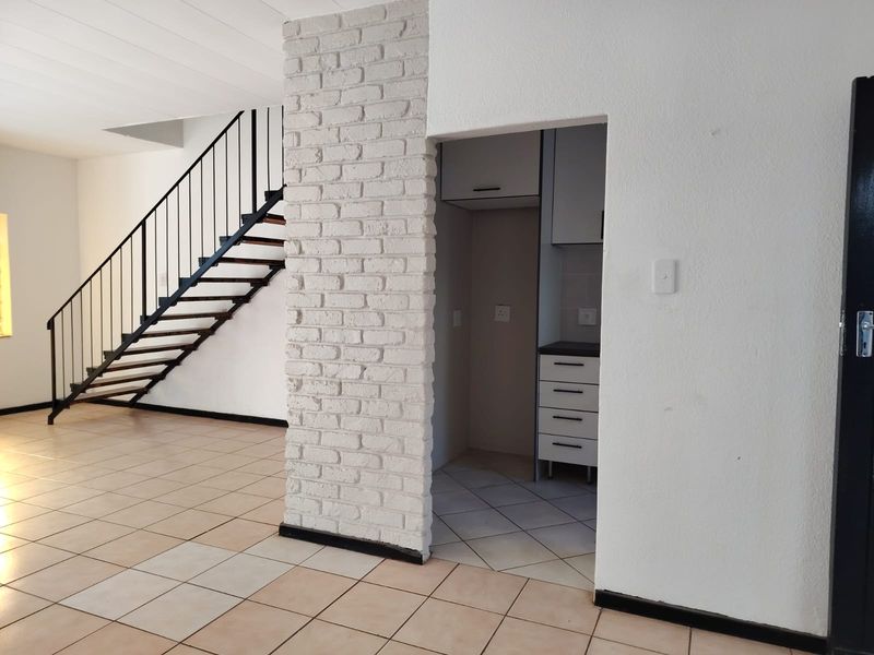 Open plan living area featuring a staircase with metal balustrade, a white painted brick feature pillar, and a compact kitchenette with built-in cabinetry.