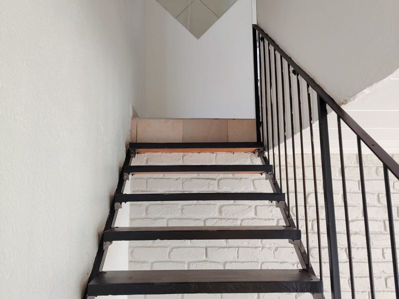A staircase featuring a metal frame and balustrade set against a painted brick wall, leading to an upper landing.