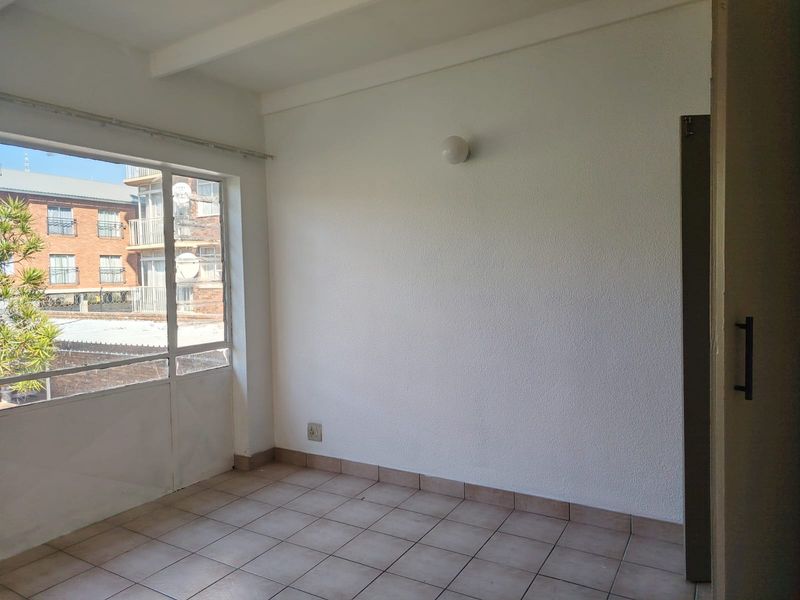 An empty bedroom featuring tiled flooring, a built-in cupboard, and a large window providing natural light and an urban view.