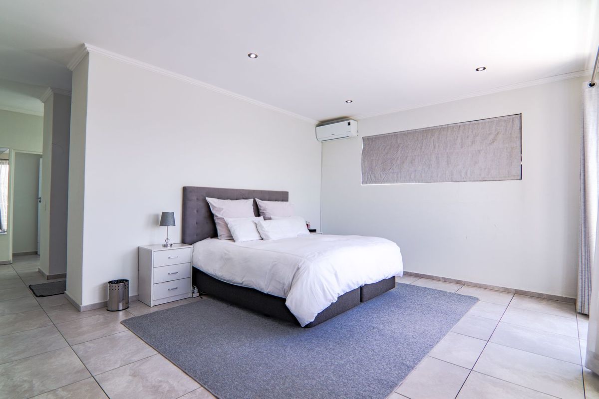 A spacious bedroom featuring neutral tiled flooring, recessed ceiling lighting, and a wall-mounted air conditioning unit.