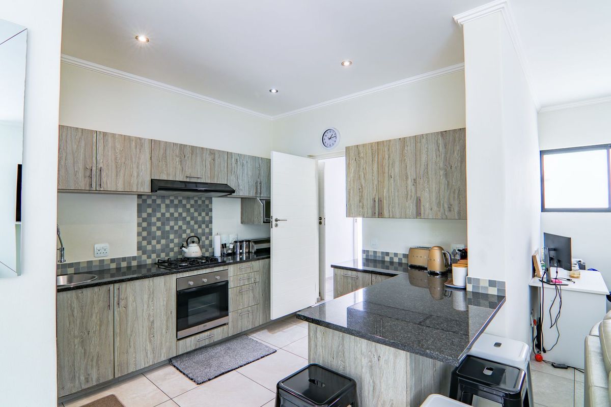 Modern kitchen featuring wood-grain cabinetry, granite countertops, a built-in oven, gas hob, and a breakfast bar island.