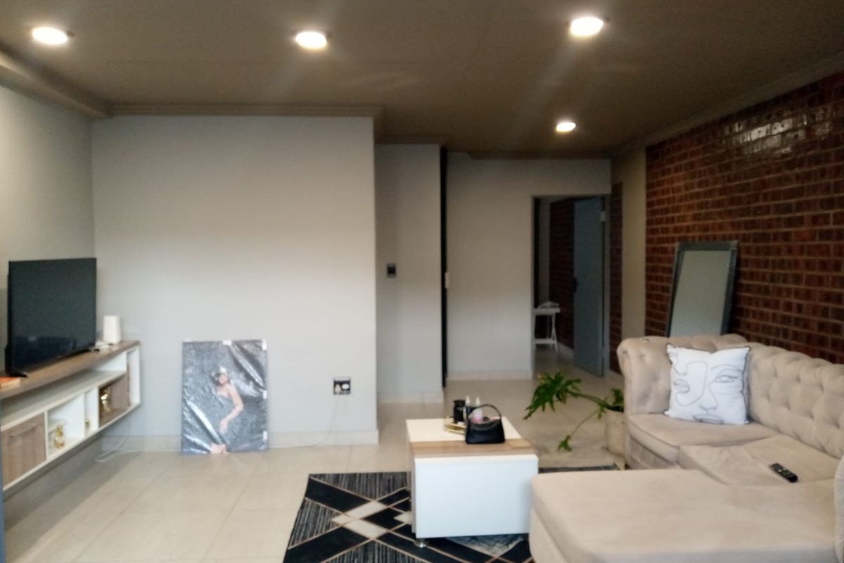 A spacious living room featuring a prominent exposed brick feature wall, tiled flooring, and recessed ceiling downlights.