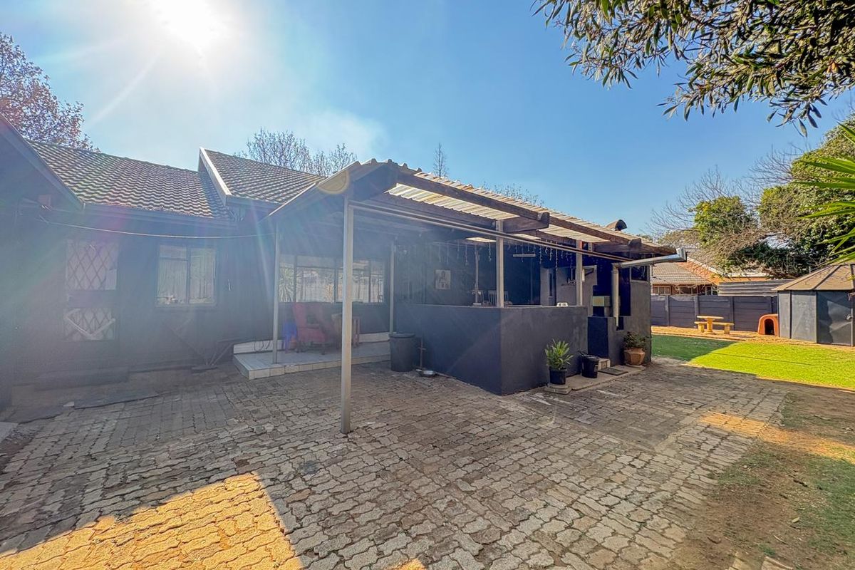 Rear view of the property featuring a covered patio area, paved outdoor space, and a built-in braai, set within a private garden.