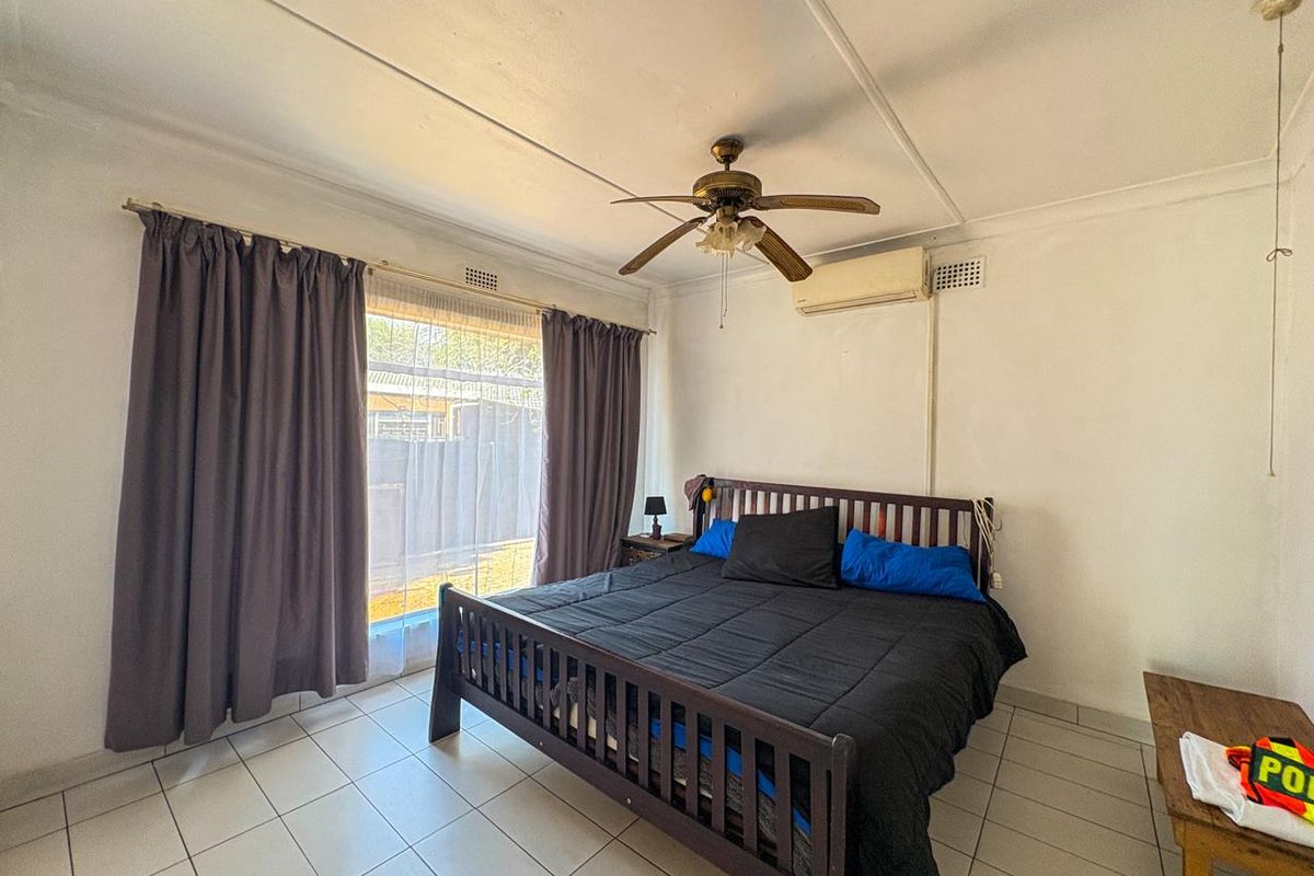 A bedroom featuring tiled flooring, a ceiling fan, and a wall-mounted split-system air conditioner, with direct access to the exterior via a sliding glass door.