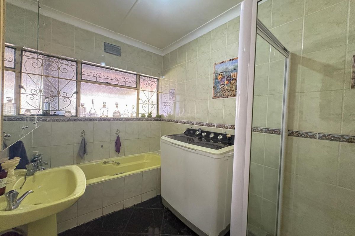 A dated bathroom featuring a yellow pedestal basin and bathtub, a separate shower enclosure, and full-height wall tiling with decorative border accents.
