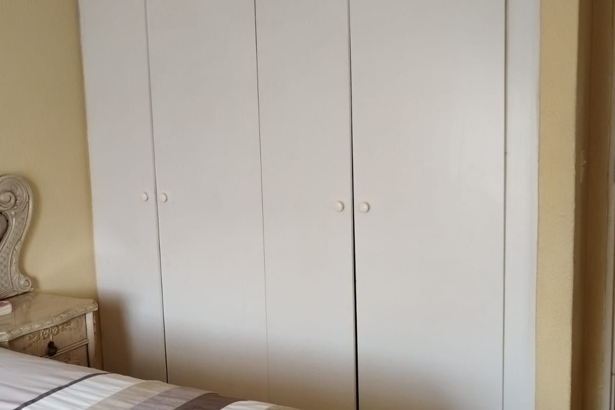 A bedroom featuring built-in white wardrobe cabinetry with simple round handles and light-toned laminate flooring.