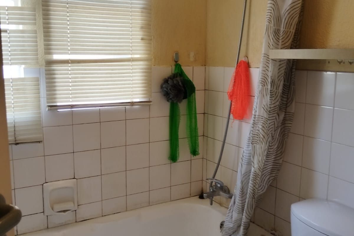 A compact bathroom featuring a bathtub with a shower attachment, a standard toilet, and white wall tiling.