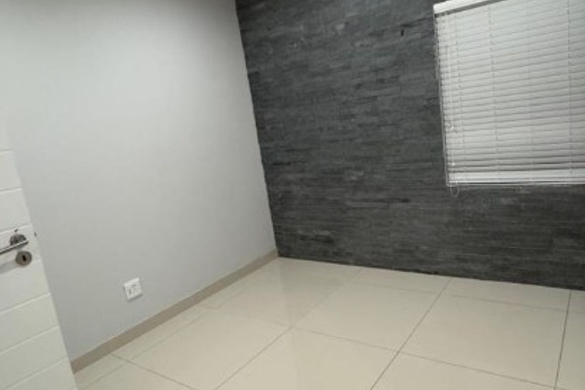 A bright, empty bedroom featuring large format floor tiles, a dark textured feature wall, and recessed ceiling lighting.