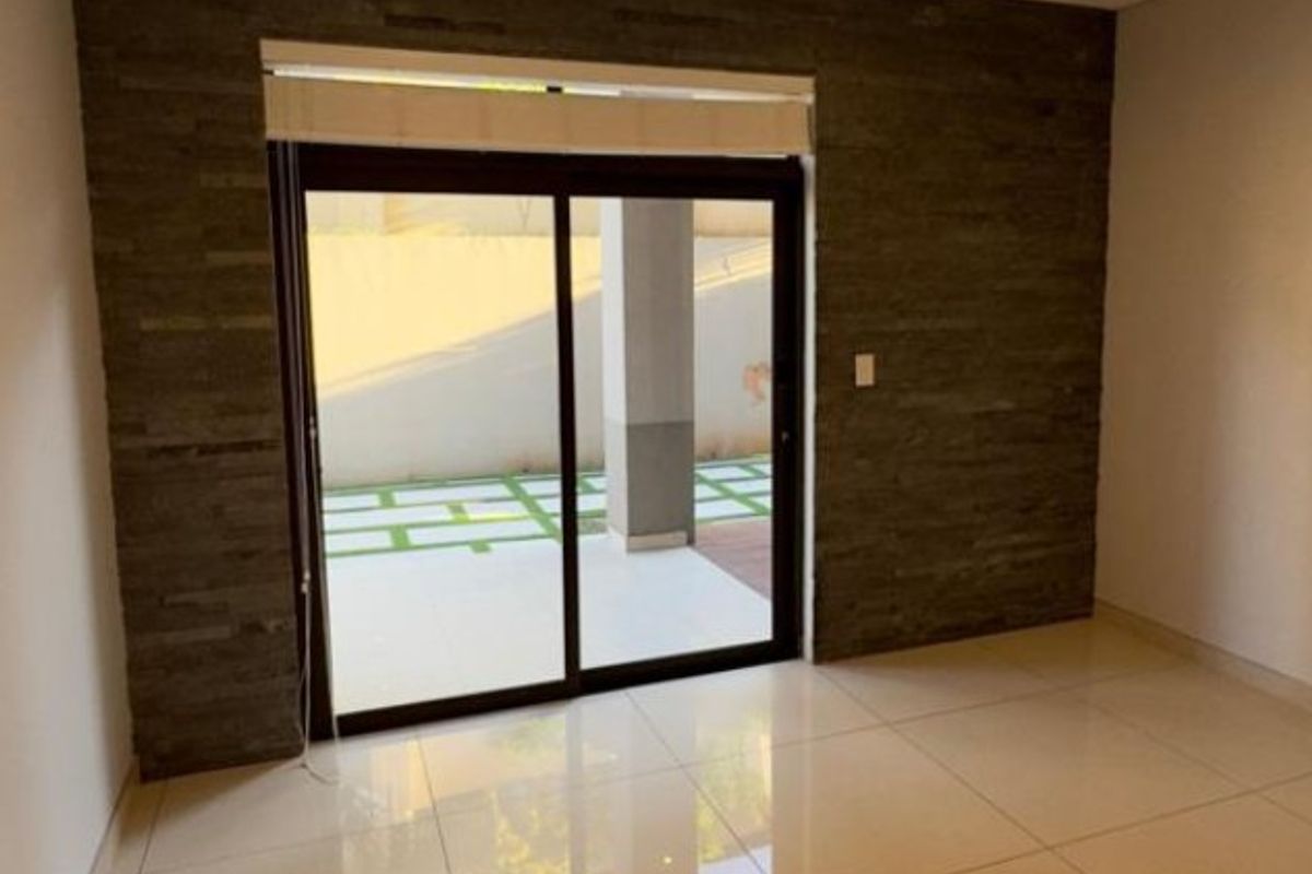 A bright, empty living area featuring large format floor tiles, a textured stone feature wall, and sliding glass doors leading to an outdoor patio.