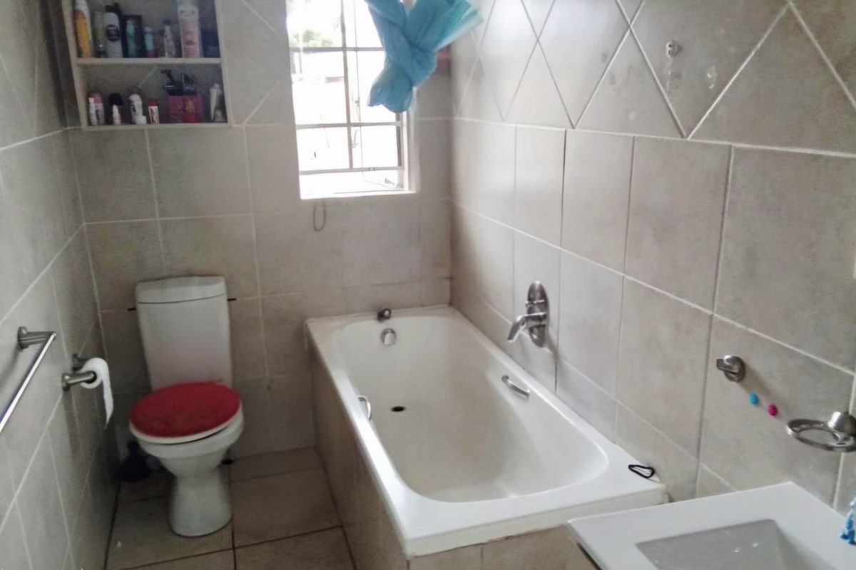 A functional bathroom featuring a built-in bathtub, wall-mounted faucet, toilet, and integrated wall shelving for storage.