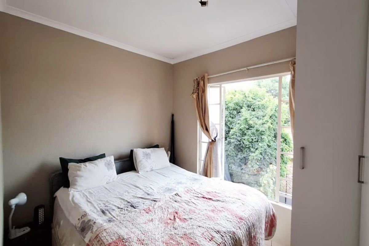 A bedroom featuring built-in cupboards and a large window providing natural light and garden views.