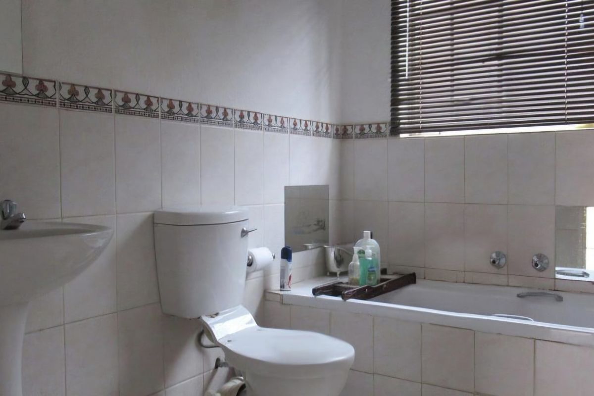 A dated bathroom featuring a pedestal basin, built-in bathtub, and tiled walls with decorative border accents, requiring cosmetic updates to modernize the space.