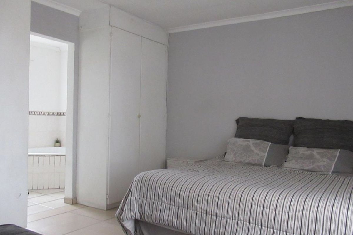 A bedroom featuring built-in cupboards and tiled flooring, with an adjoining bathroom visible through the doorway.
