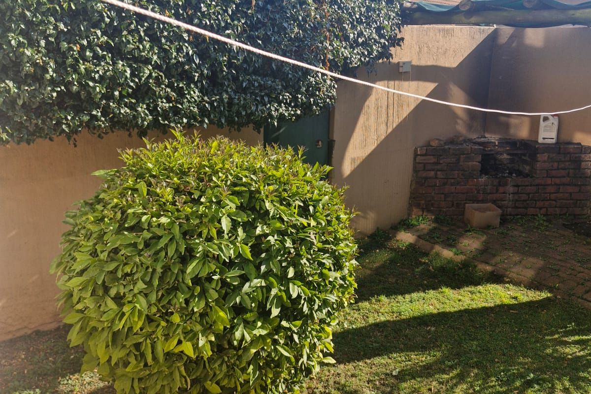 A private rear garden area featuring a brick built-in braai, established perimeter hedging, and a lawn space.