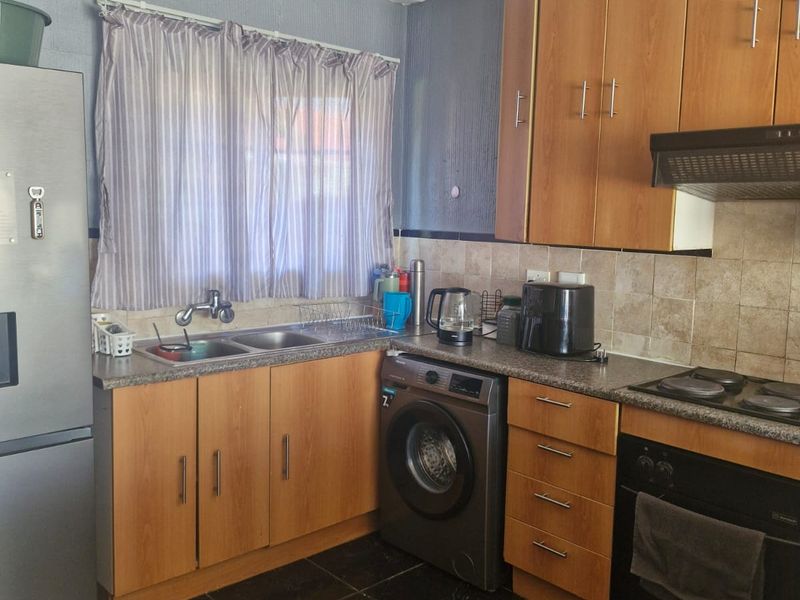 Functional kitchen featuring laminate cabinetry, granite countertops, built-in oven, electric hob, extractor fan, and integrated washing machine with tiled backsplash and flooring.